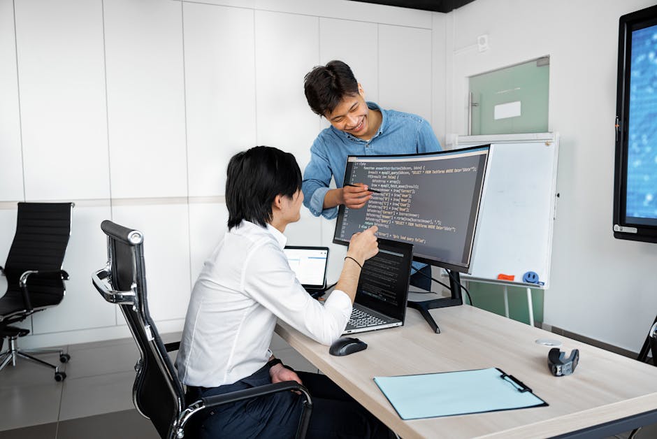 Two developers collaborating at a desk with laptops in a small team startup environment