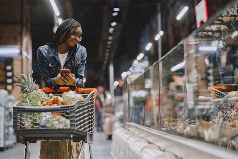 A young woman with afro braids grocery shopping in a supermarket, using a mobile phone.